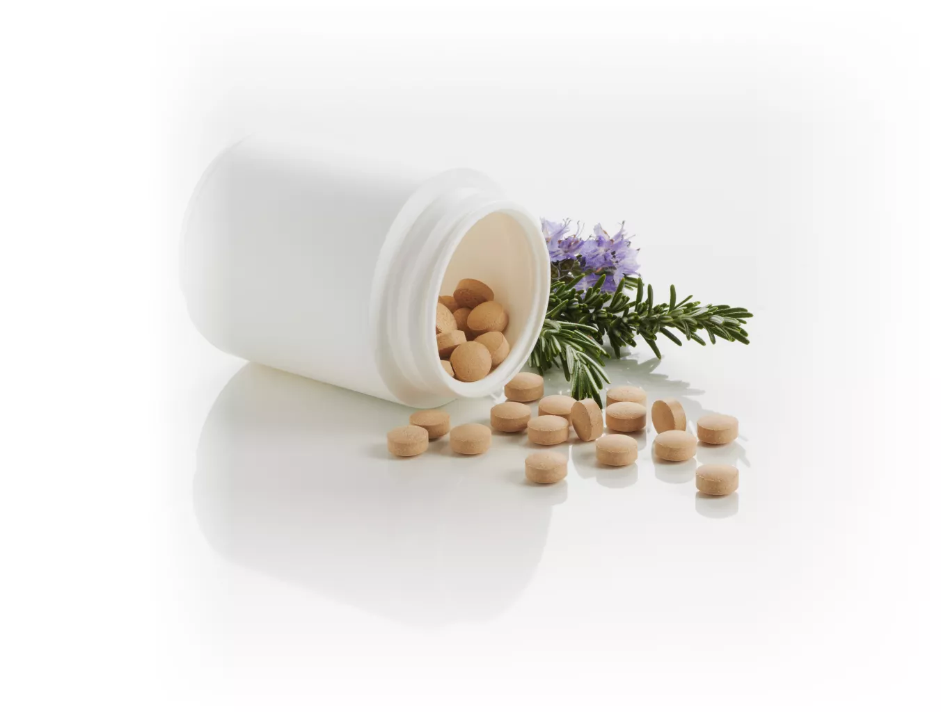 White pill box in upside-down HDPE with beige tablets inside and on the floor, next to small flowers.